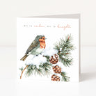 A square greeting card with a white background, featuring a watercolour illustration of a robin bird perched on a snowy pine branch with pinecones. The text 'all is calm all is bright' appears above the bird in black and coral script.