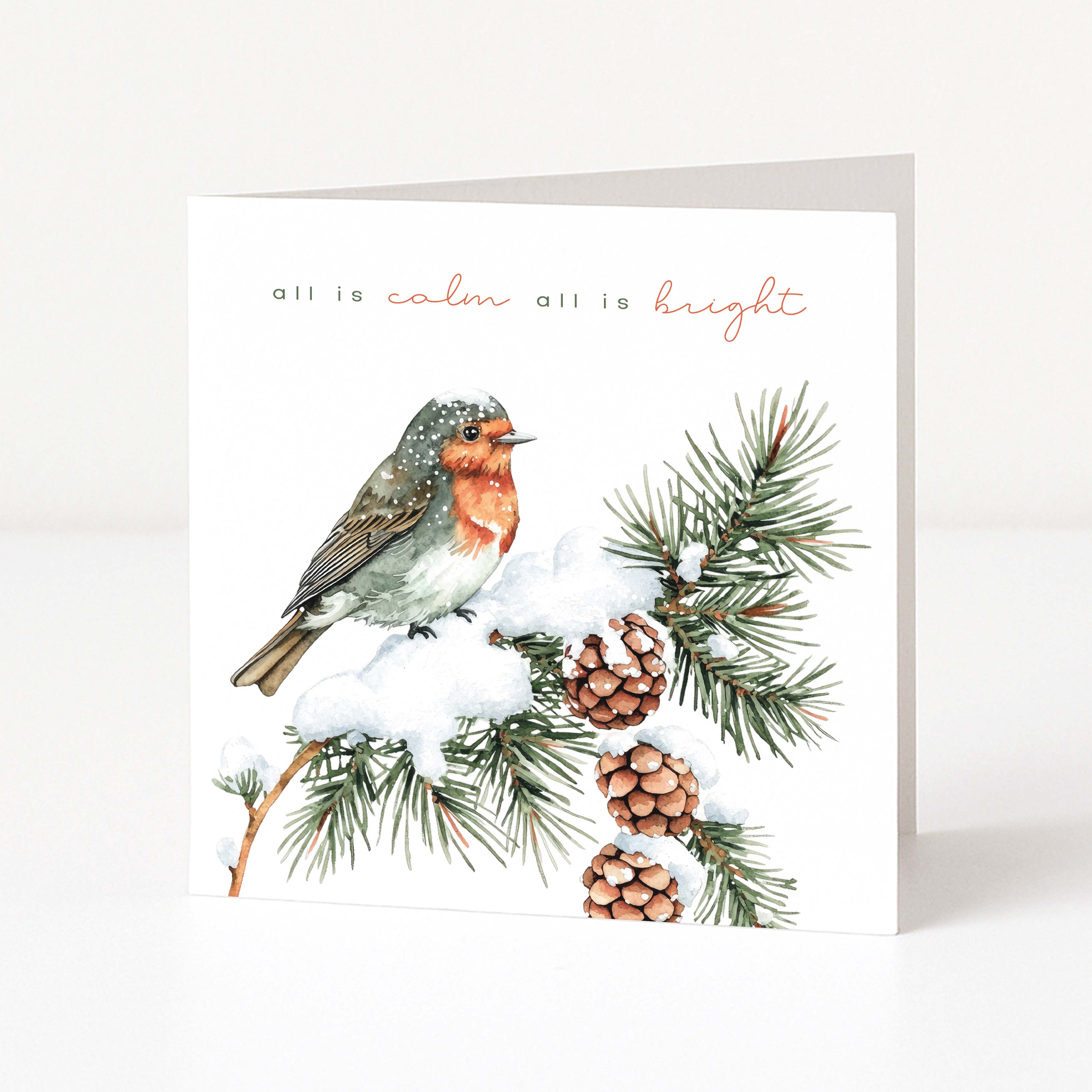 A square greeting card with a white background, featuring a watercolour illustration of a robin bird perched on a snowy pine branch with pinecones. The text 'all is calm all is bright' appears above the bird in black and coral script.
