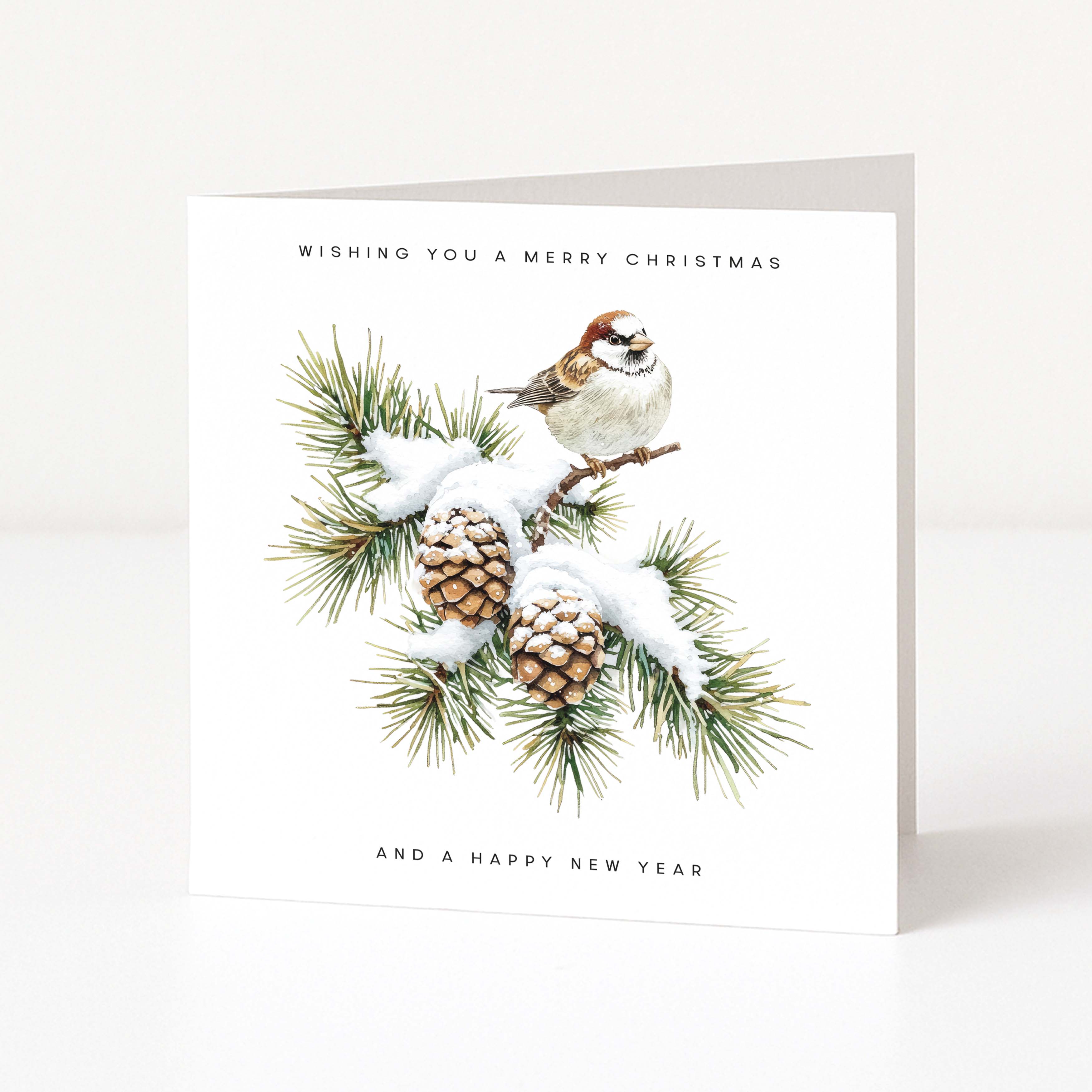 A square white Christmas greeting card standing upright on a light neutral surface. The front features an illustration of a small brown-and-white bird perched on a snow-dusted pine branch with pinecones, with the text 'WISHING YOU A MERRY CHRISTMAS' at the top and 'AND A HAPPY NEW YEAR' at the bottom.