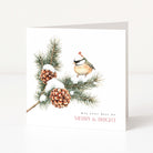 A square white Christmas greeting card standing upright on a light neutral surface. The front features an illustrated pine branch with snow, two pinecones, and a small bird, with the text 'may your days be MERRY & BRIGHT' near the bottom.