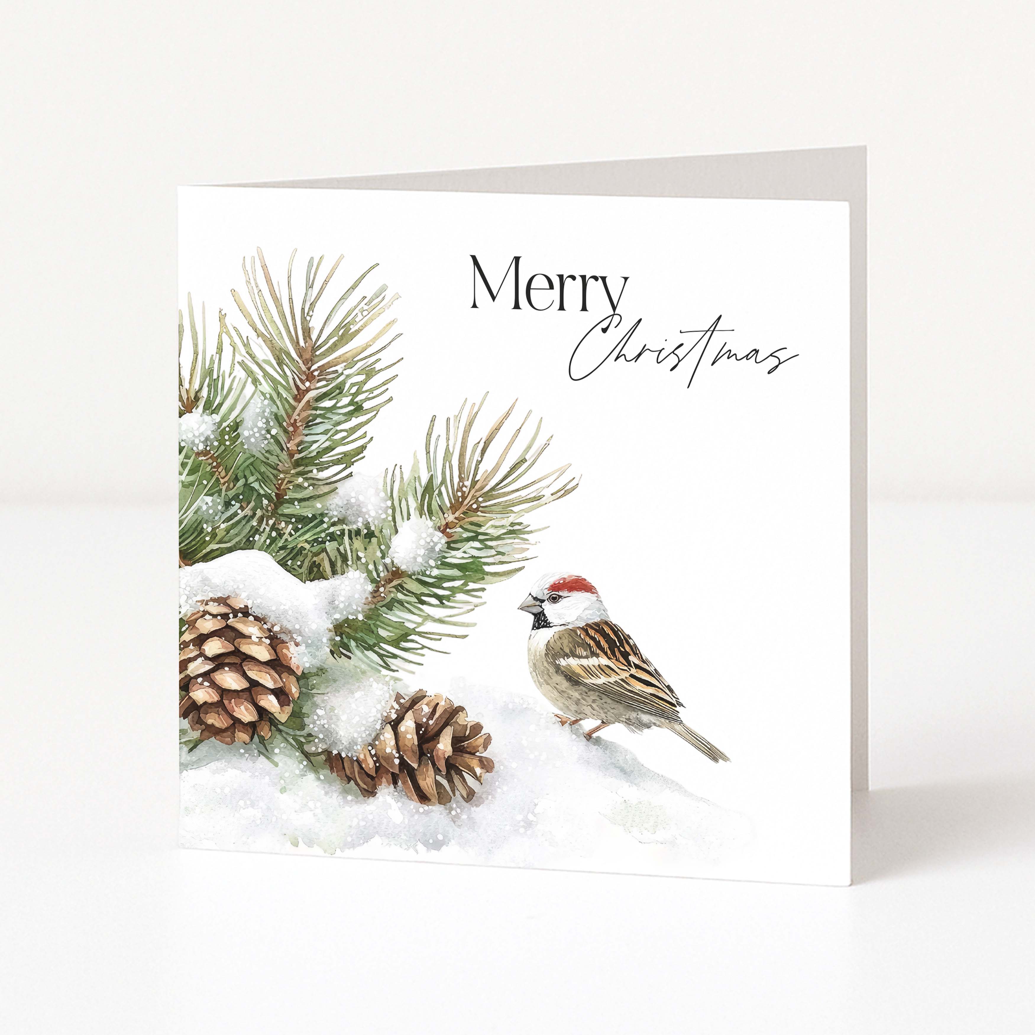 A square Christmas greeting card standing upright on a white surface. The card features a watercolour-style winter scene with pine branches covered in snow, two pinecones, and a small bird.