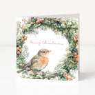 A square Christmas greeting card featuring a watercolor robin bird framed by a green pine wreath with red berries, on a white background with the words 'Merry Christmas' in pink script.