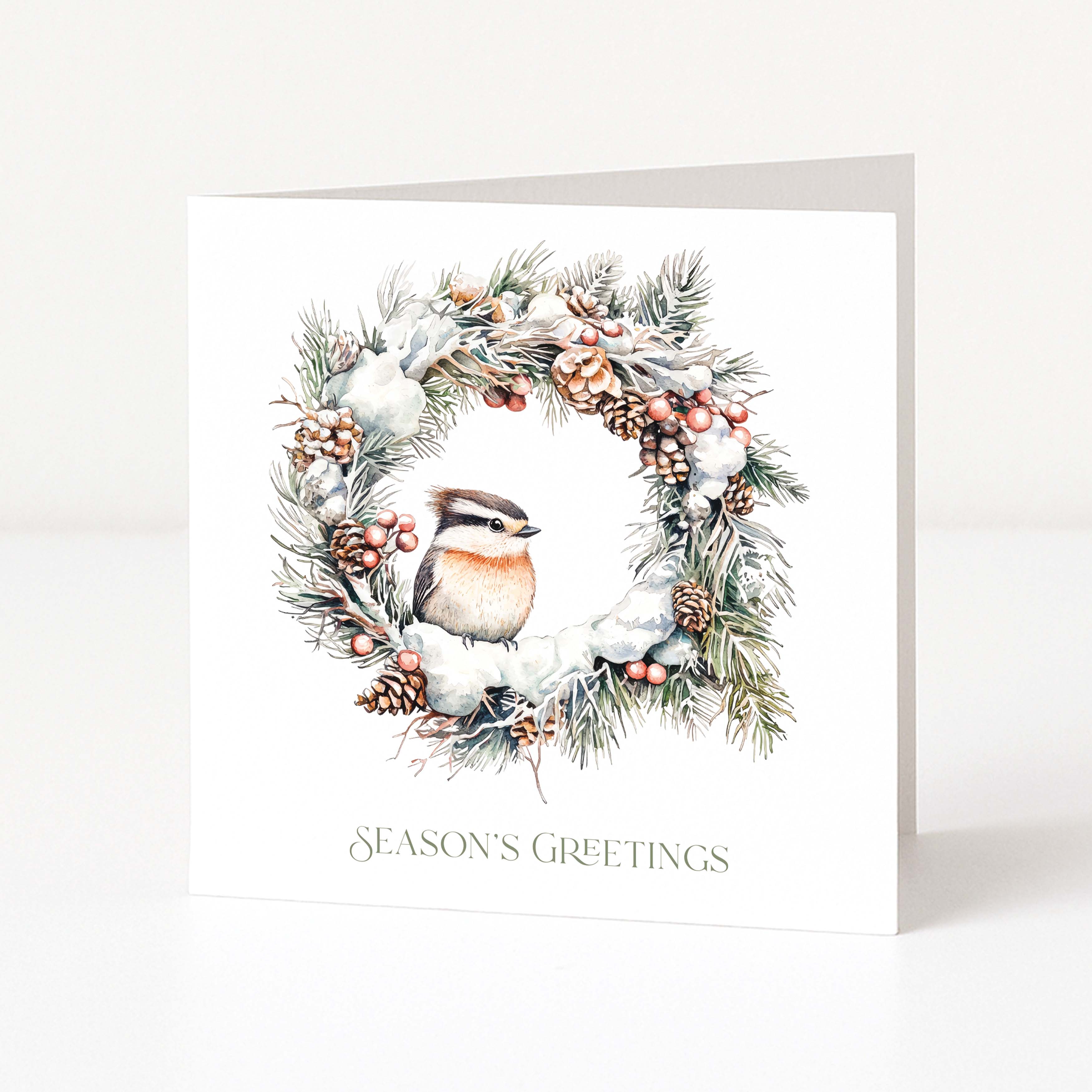 A white square Christmas greeting card standing upright on a light grey surface, featuring a winter wreath illustration with a small bird, pinecones, berries, and the text 'SEASON'S GREETINGS' at the bottom.
