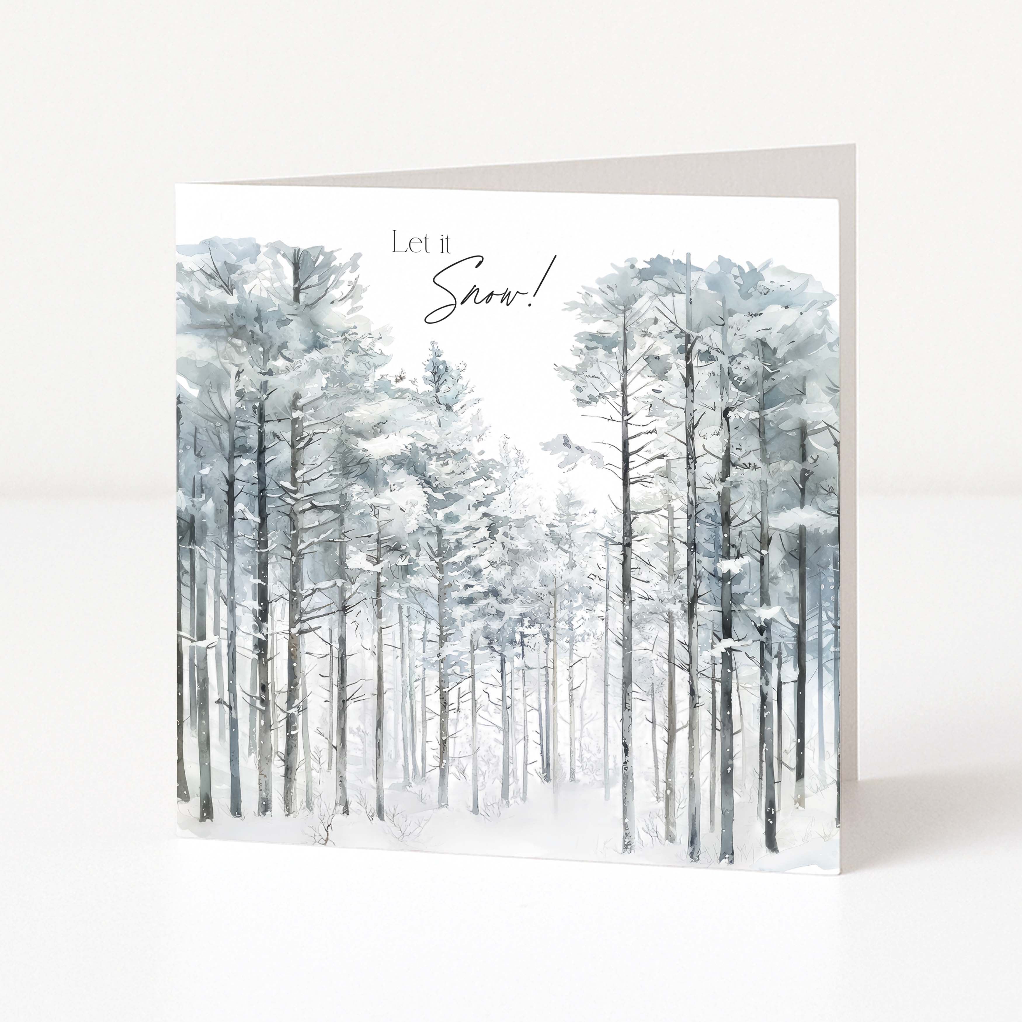 A square Christmas greeting card standing upright on a white surface, featuring a watercolour winter forest scene with tall snow-covered trees and the text 'Let it Snow!' at the top.