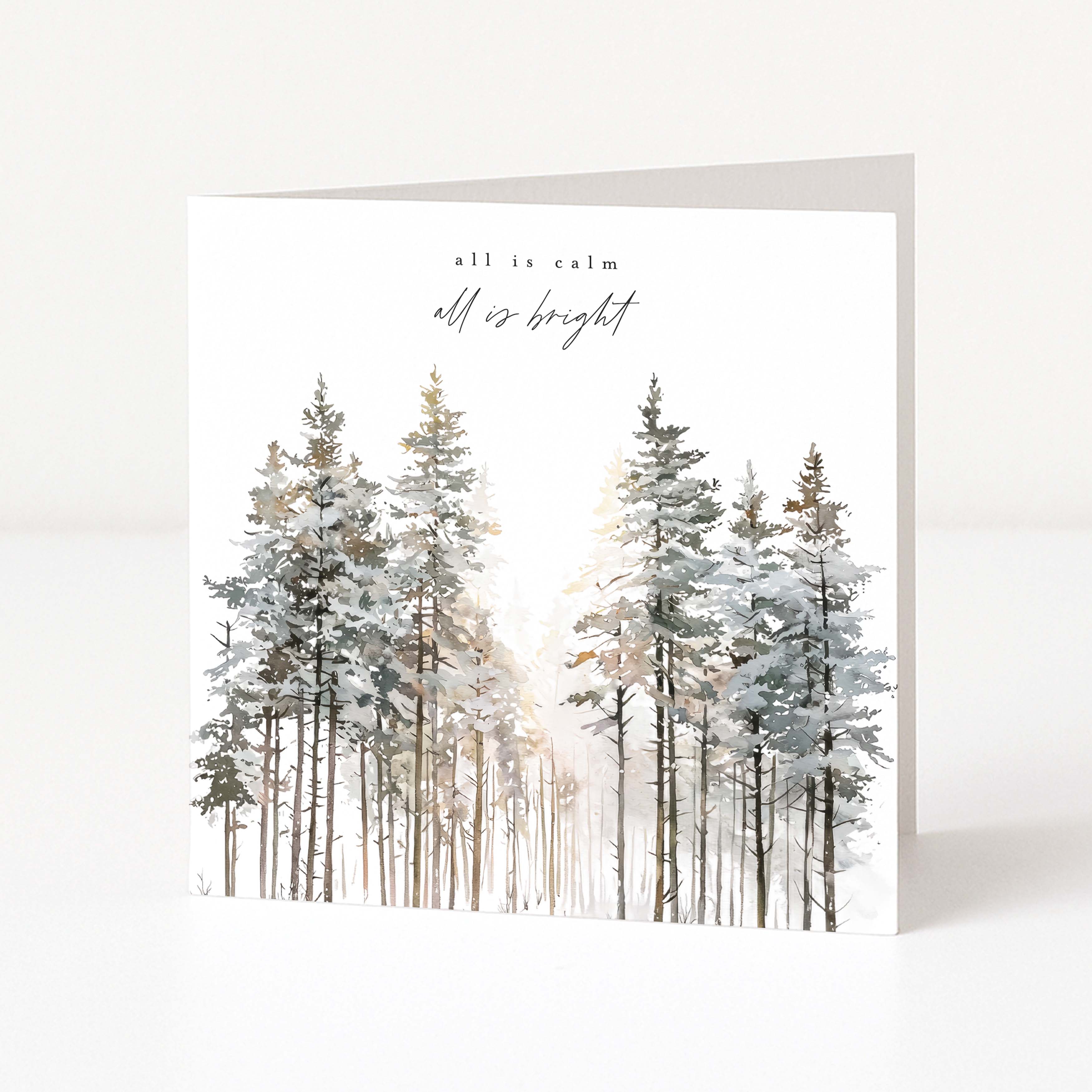 A square Christmas greeting card standing upright on a white surface, featuring a watercolor winter forest with snow-covered pine trees and the words 'all is calm all is bright' at the top.