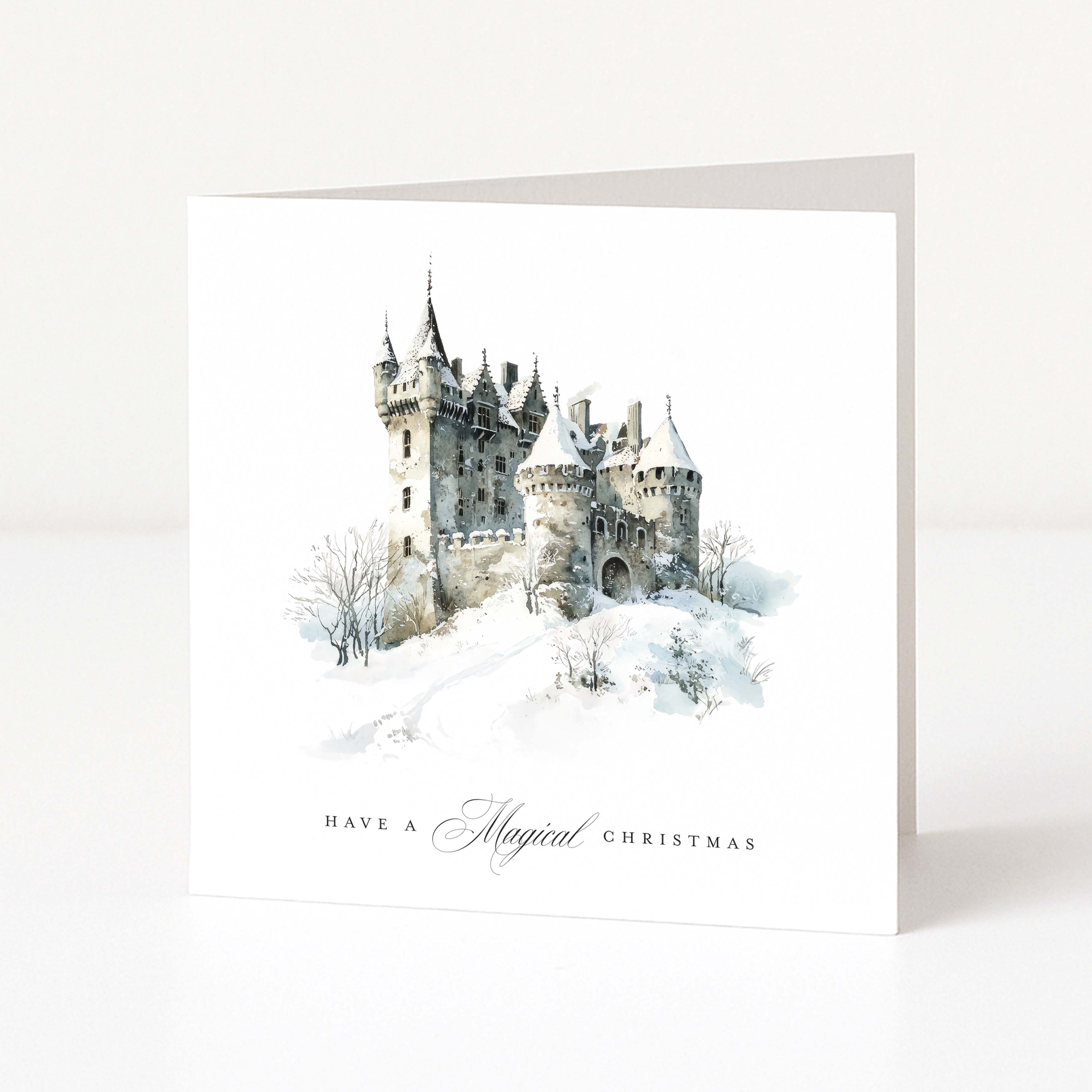 A white Christmas greeting card standing upright, featuring a watercolour illustration of a snowy castle with the text 'HAVE A Magical CHRISTMAS' printed below.
