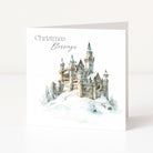 A square Christmas greeting card standing upright on a white surface. The front of the card shows a watercolor-style illustration of a snowy castle with the words 'Christmas Blessings' printed above it.