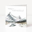 A square Christmas greeting card standing upright on a white surface, featuring a watercolor-style winter mountain landscape with snow-covered peaks and a winding stream. The text at the top reads, 'Walking in a Winter Wonderland.