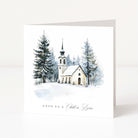 A white Christmas greeting card showing a watercolour church and surrounding forest scene and "Unto us a child is born" text beneath