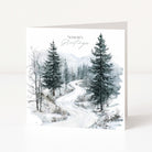 A square Christmas greeting card standing upright on a white surface, featuring a winter landscape illustration with snow-covered trees and a winding road. The card reads 'Season's Greetings' in elegant script near the top.