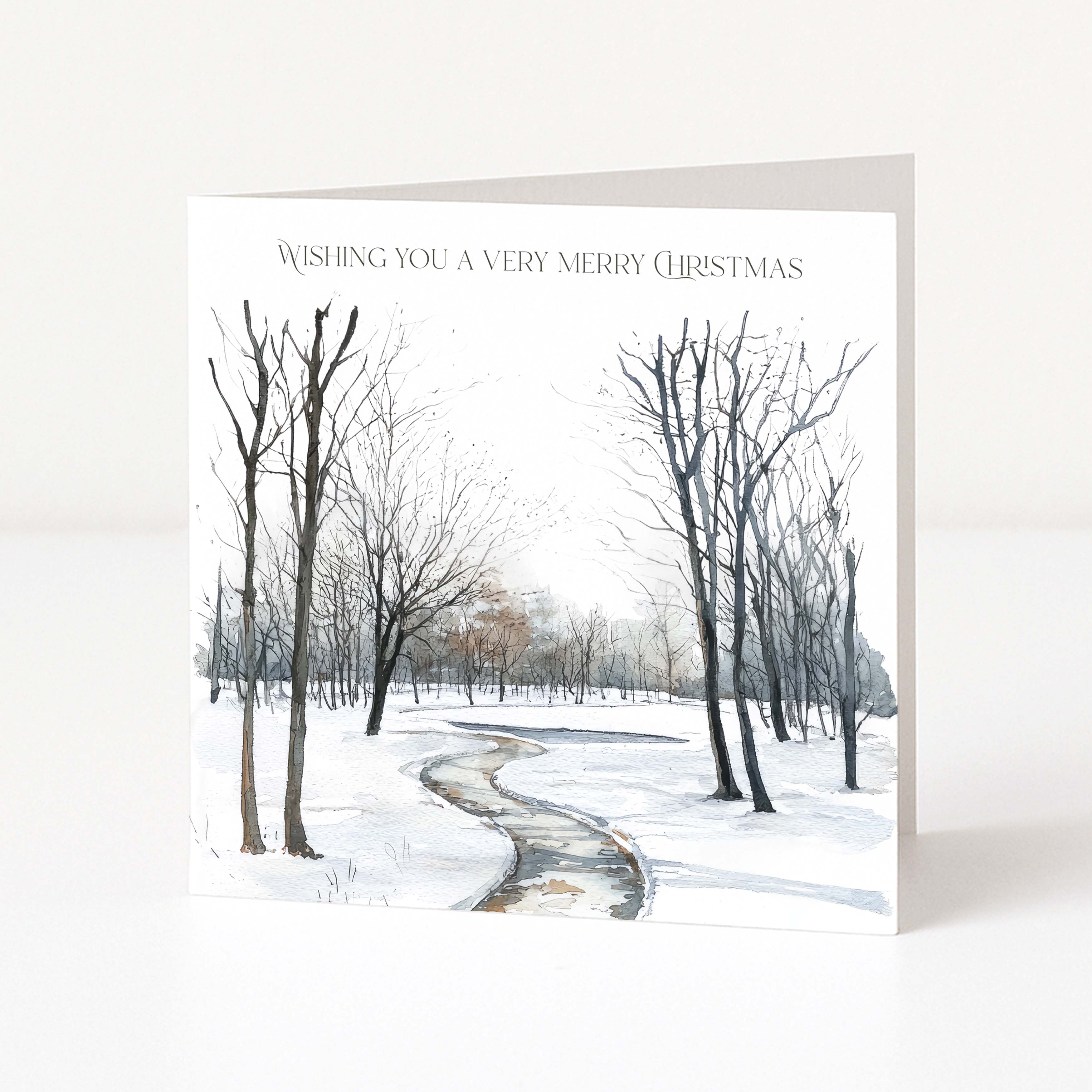 A square Christmas greeting card standing upright on a white surface. The card features a watercolor winter landscape with bare trees, snow, and a winding path, with the text 'WISHING YOU A VERY MERRY CHRISTMAS' printed at the top.