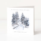 A square white Christmas greeting card standing upright on a light neutral surface. The front features a watercolor-style winter forest scene with snow-covered evergreen trees and a winding path, with the text 'we wish you a merry christmas' at the top and 'and a happy new year' at the bottom.