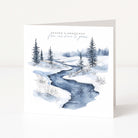 A square Christmas greeting card standing upright on a white surface, featuring a watercolor winter landscape with a winding blue stream, snow-covered ground, evergreen trees, and the text 'Season's Greetings' and 'from out of time to greet.'.