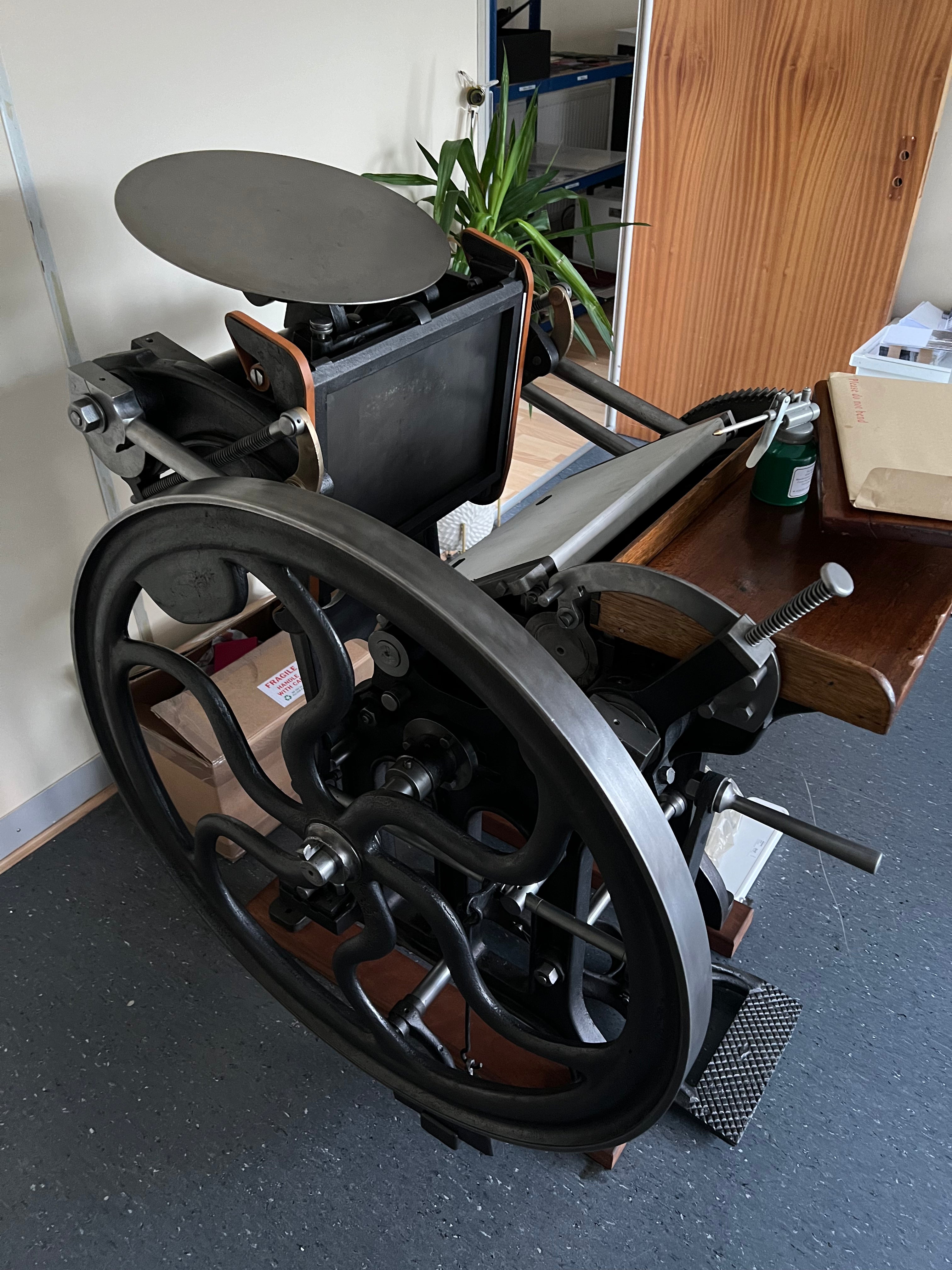 Vintage letterpress printing press in a room with boxes and a plant