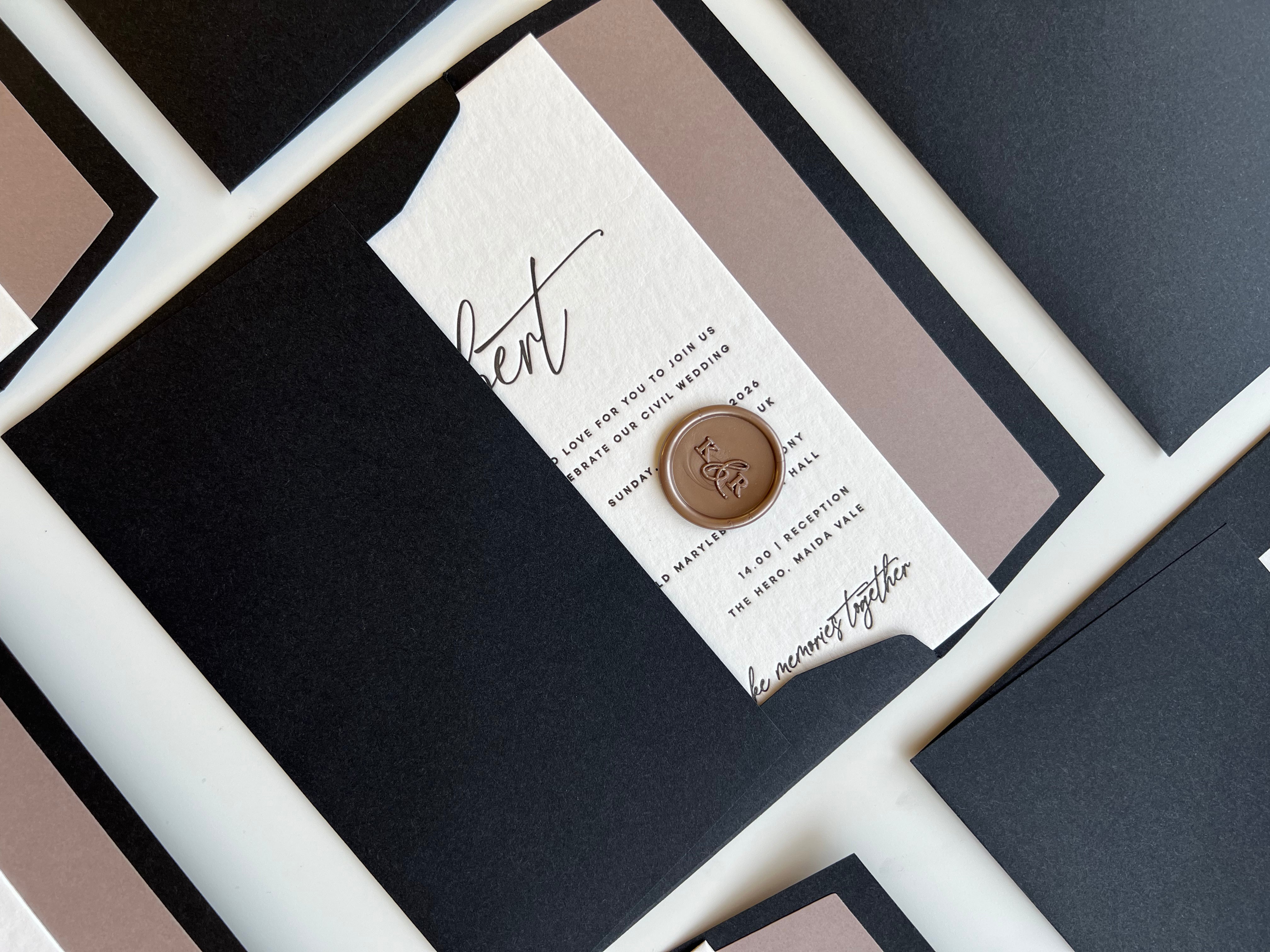 Black envelope with a letterpressed invitation card featuring cursive text and a wax seal, surrounded by other black lined envelopes.