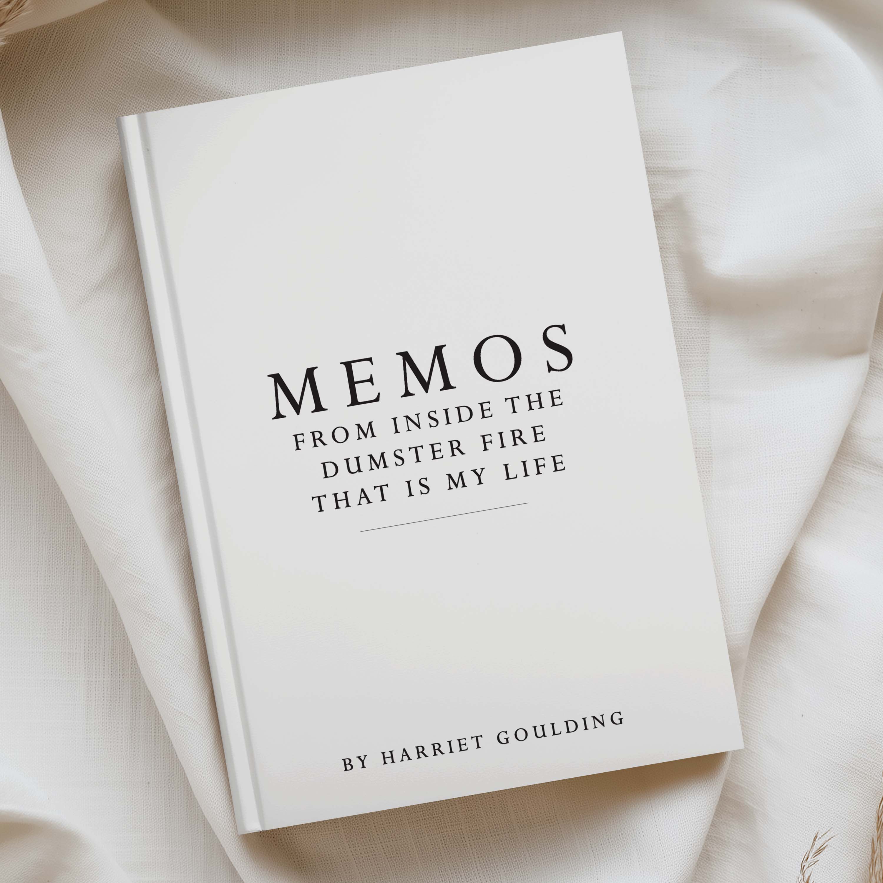 A hardcover book titled 'MEMOS FROM INSIDE THE DUMSTER FIRE THAT IS MY LIFE' by Harriet Goulding, placed on draped cream-colored fabric.