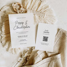 A styled flat-lay of wedding stationery on a neutral fabric surface. Two white cards are shown: a main invitation reading 'Poppy & Christopher' with wedding details, and a separate 'happy response' card with a QR code.