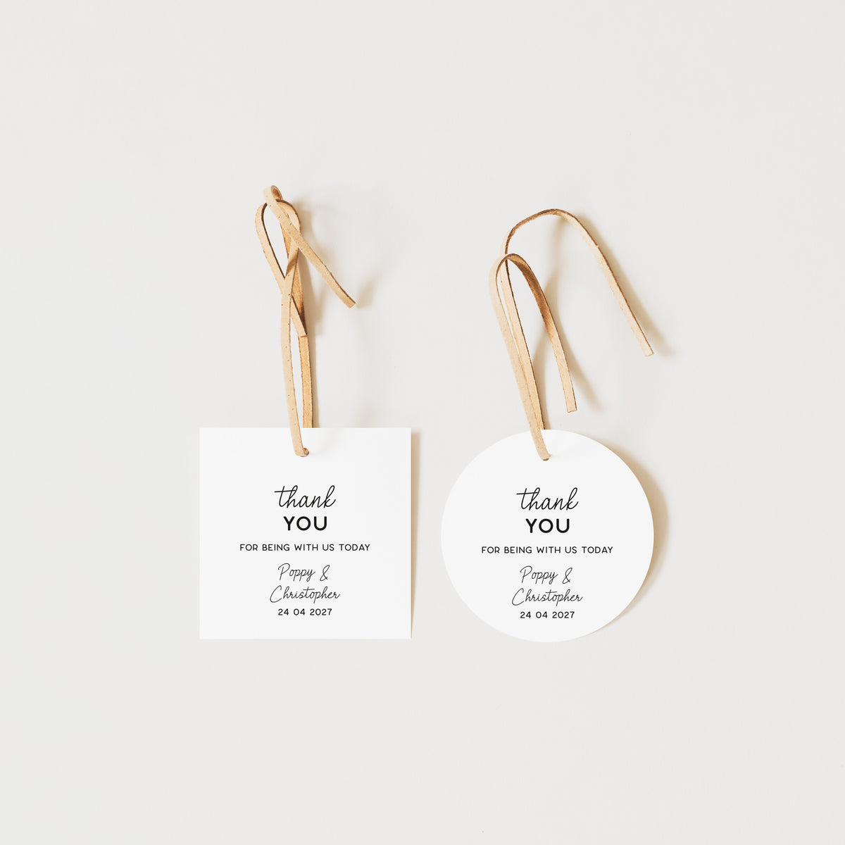 Two personalised thank you favours on a light grey background: a rectangular white card with a tan string and a round white tag with a tan string, both printed with the words 'thank you' and custom names/date text.