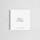 A white wedding guest book with names of couple, wedding date and wedding venue, with black ring binder