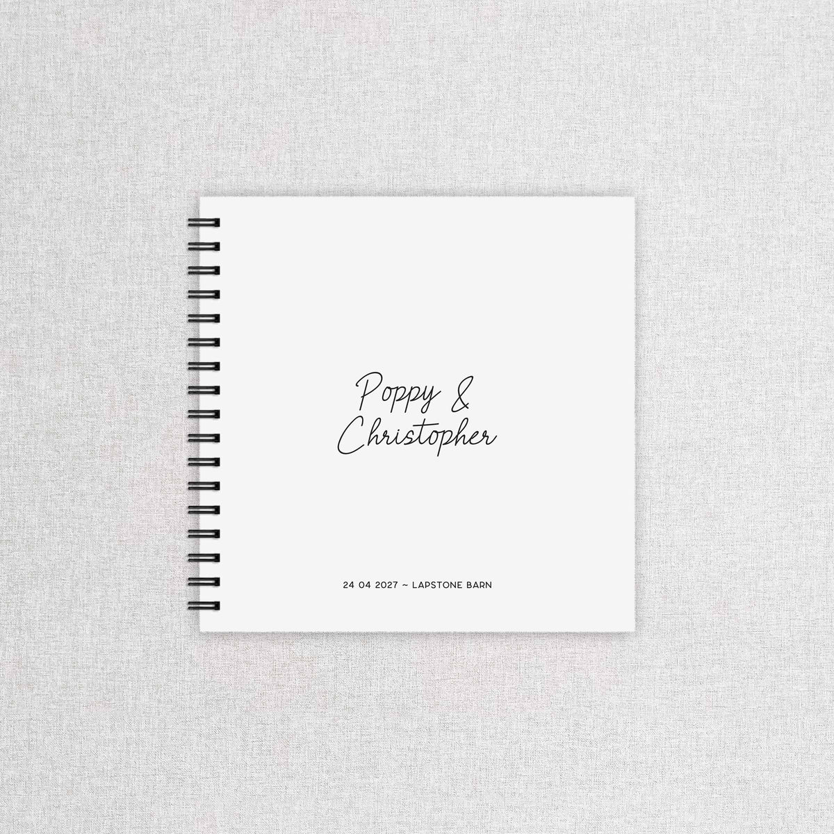 A white wedding guest book with names of couple, wedding date and wedding venue, with black ring binder