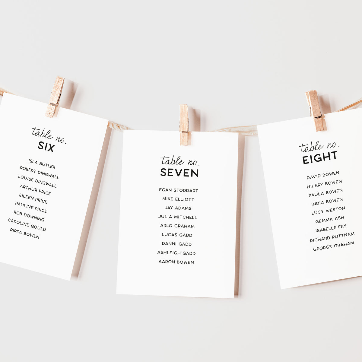 Three vertical white cards with printed table numbers hang from a string between two wooden clothespins against a light gray background.