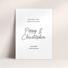 A minimalist white wedding welcome sign with black text reading 'Welcome to our happily ever after.', names and wedding date and venue.