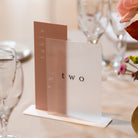 Table number 'two' on a stand with floral arrangement and glasses in the background