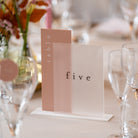 Table number 'five' on a stand with floral decorations and glasses in the background