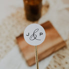 Close-up of a round white sticker with 'J & P' on a wooden stick, blurred background