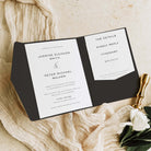 Pocketfold Wedding invitation set on a textured surface with a gold pen and white flowers.