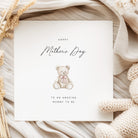 Greeting card with teddy bear illustration and 'Happy Mother's Day' text on a soft fabric background.
