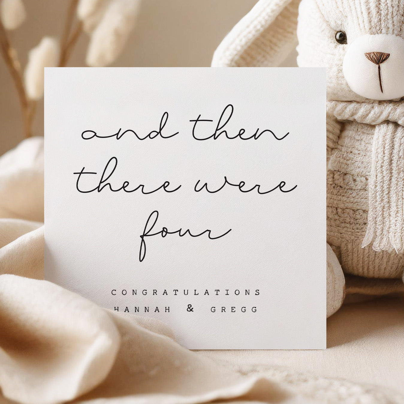 Card with 'and then there were four' text, surrounded by soft textures and a teddy bear.