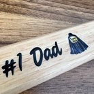Wooden bat with '#1 Dad' and 'Super Dad' stickers on a wooden surface