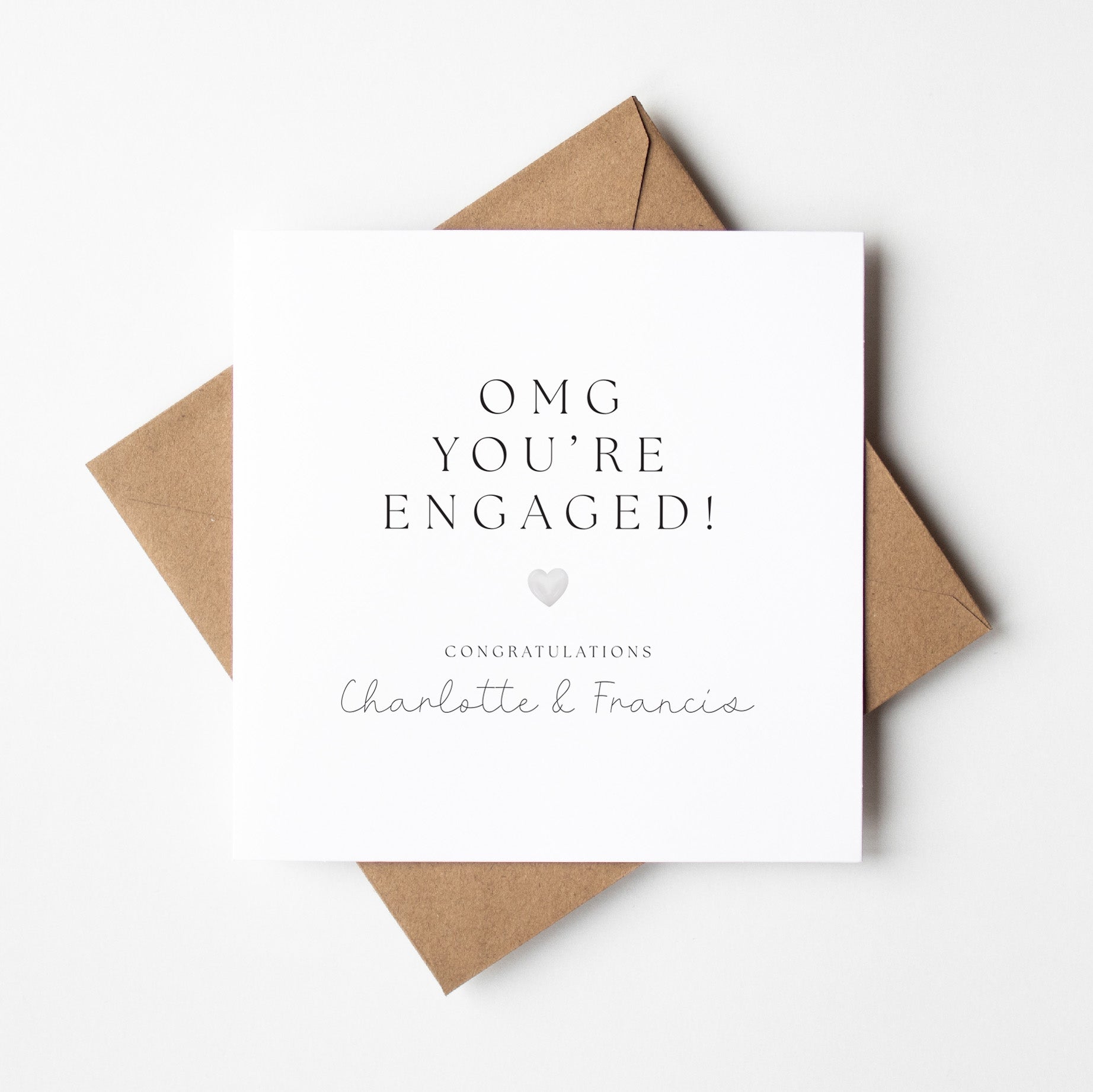 Engagement card with 'OMG YOU'RE ENGAGED!' text and a heart symbol, placed on a white background.