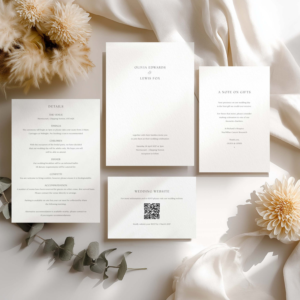 A coordinated flat lay of four white stationery cards with elegant serif typography, arranged on draped satin with cream flowers and greenery. The cards appear to be wedding or memorial invitation/notice stationery, including details, a note on gifts, and a website card.