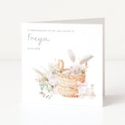 Newborn baby card with a bunny in a basket and floral elements on a white background