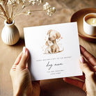 Hand holding a Mother's Day card with a dog illustration on a wooden surface.