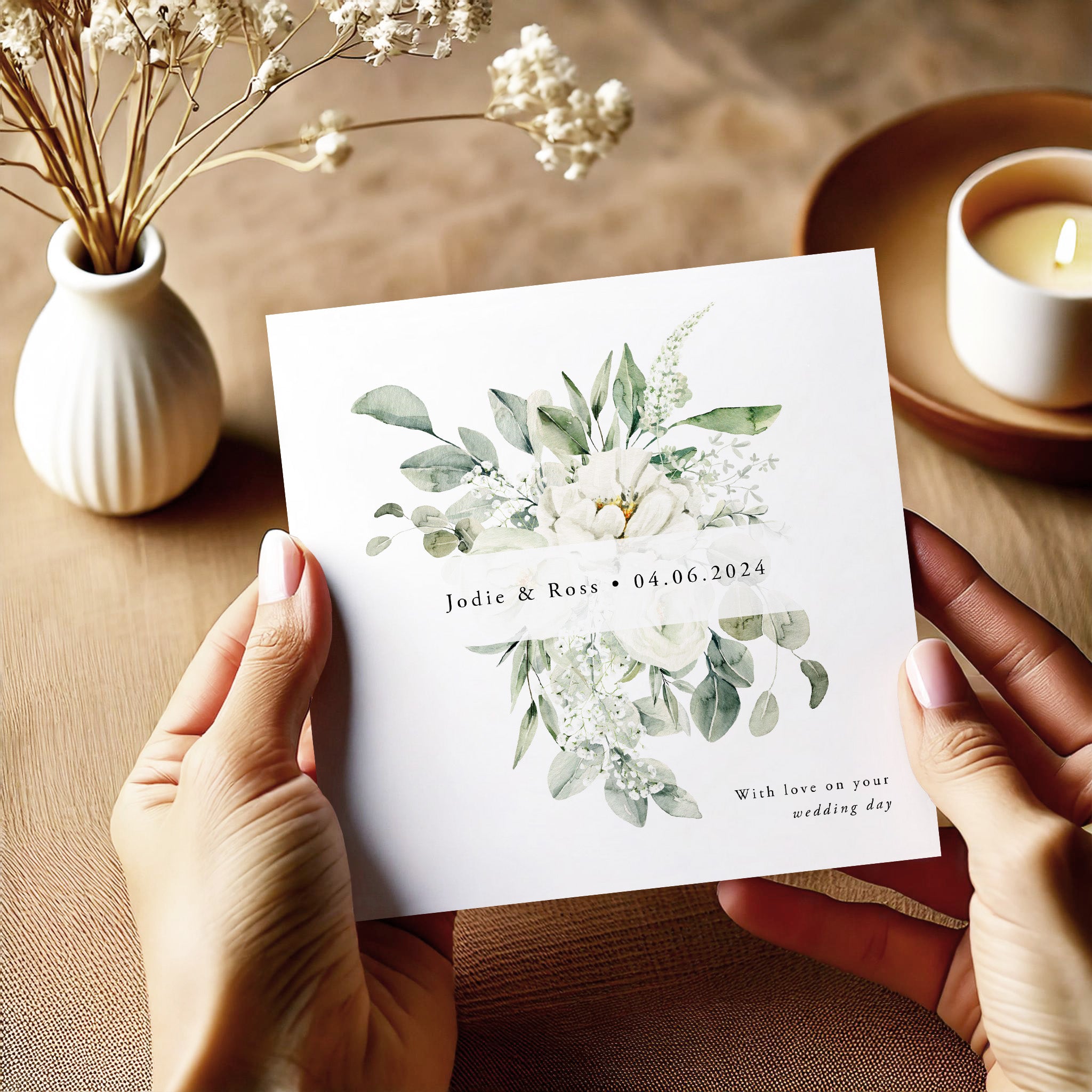 Person holding a wedding invitation card with floral design and text on a wooden table.