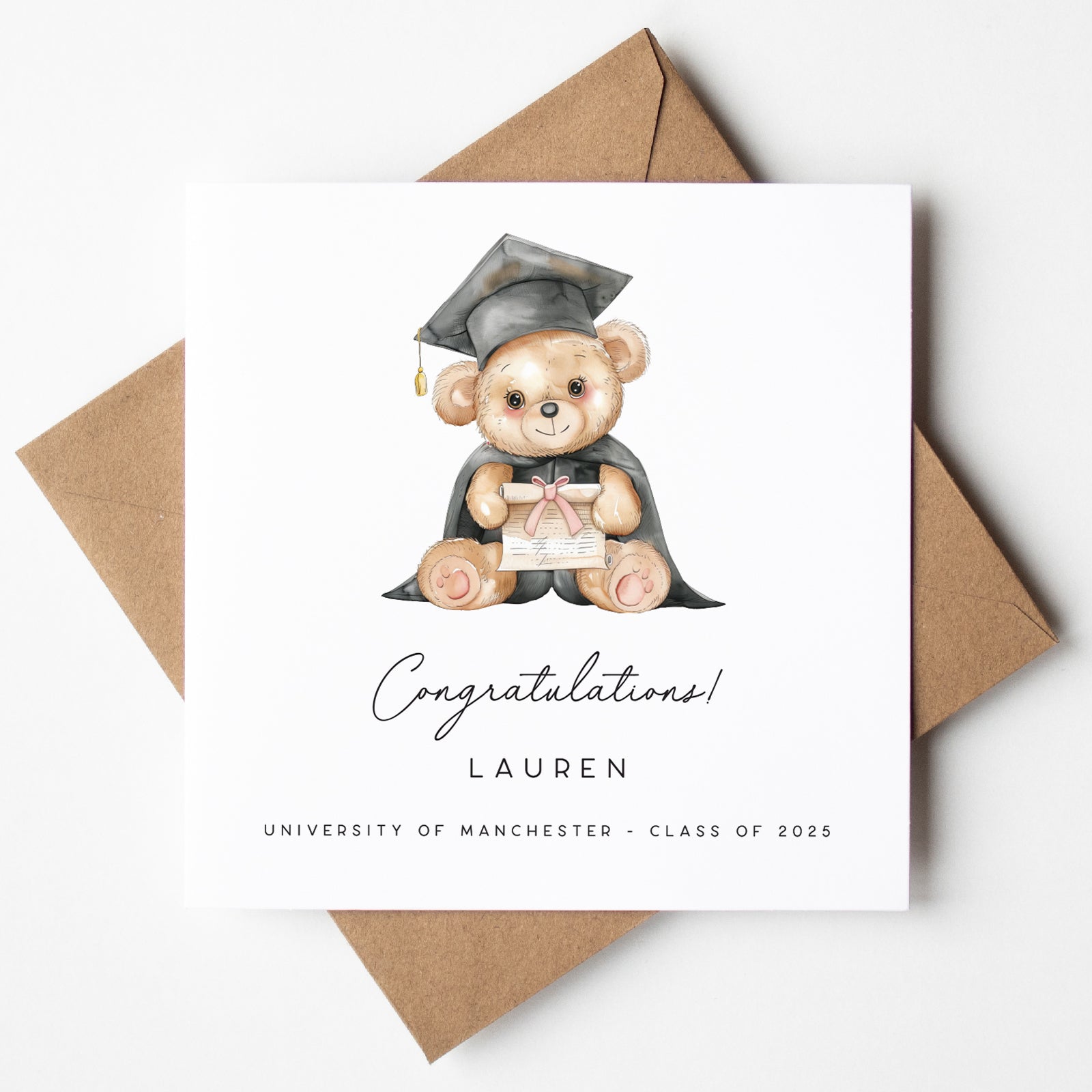 Graduation-themed card with a teddy bear in a cap and gown, surrounded by brown envelopes on a white background.