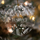Decorative ornament with floral patterns and 'HARRETT' text against a blurred Christmas tree background.
