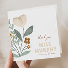 Greeting card with floral design and text held by a hand on a neutral background