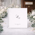 Personalized wedding guest book with monogram on a decorative table with flowers and cards.