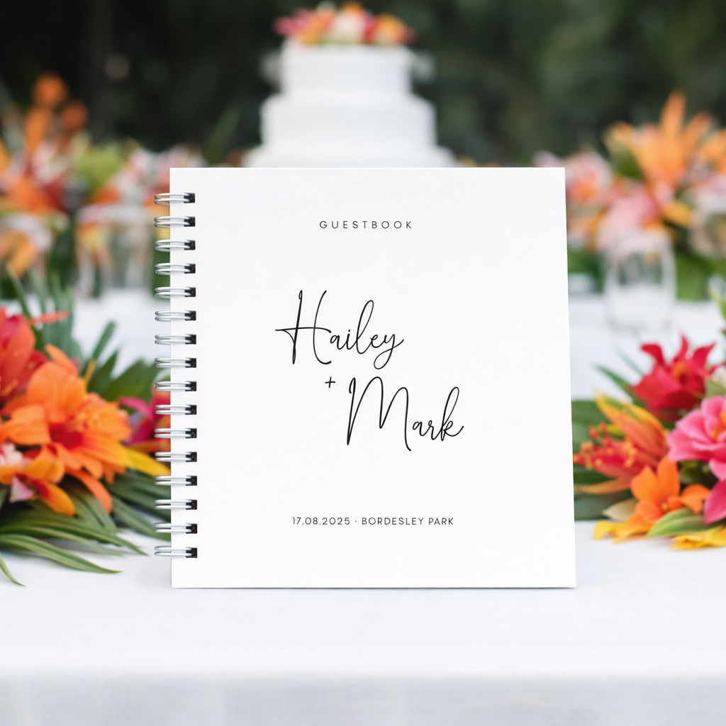Guestbook with 'Hailey + Mark' on a table with flowers and a cake in the background
