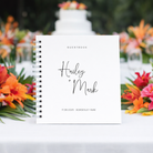Guestbook with 'Hailey + Mark' on a table with flowers and a cake in the background