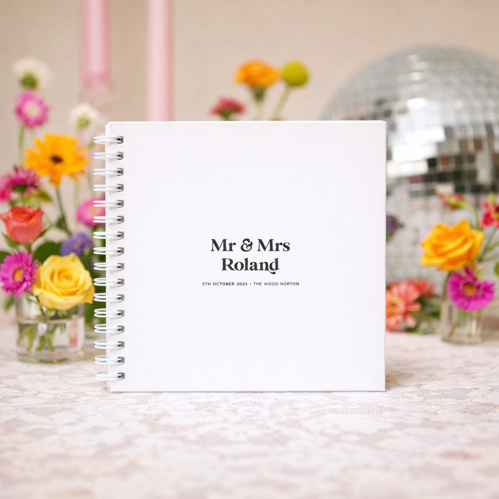 White guestbook with 'Mr & Mrs Roland' text, surrounded by colorful flowers and a disco ball.