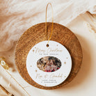 A personalized Christmas ornament displayed on a round wooden stand. The ornament is white with gold script text reading 'Merry Christmas to our special Non & Grandad' and a photo of a grandfather and grandmother, with the names 'Love Freya + Charlotte' below.
