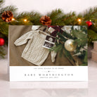 Christmas card with baby announcement featuring a sweater and photo, surrounded by festive decorations.