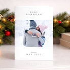 Baby announcement card with a couple holding a ultrasound photo, surrounded by Christmas decorations.
