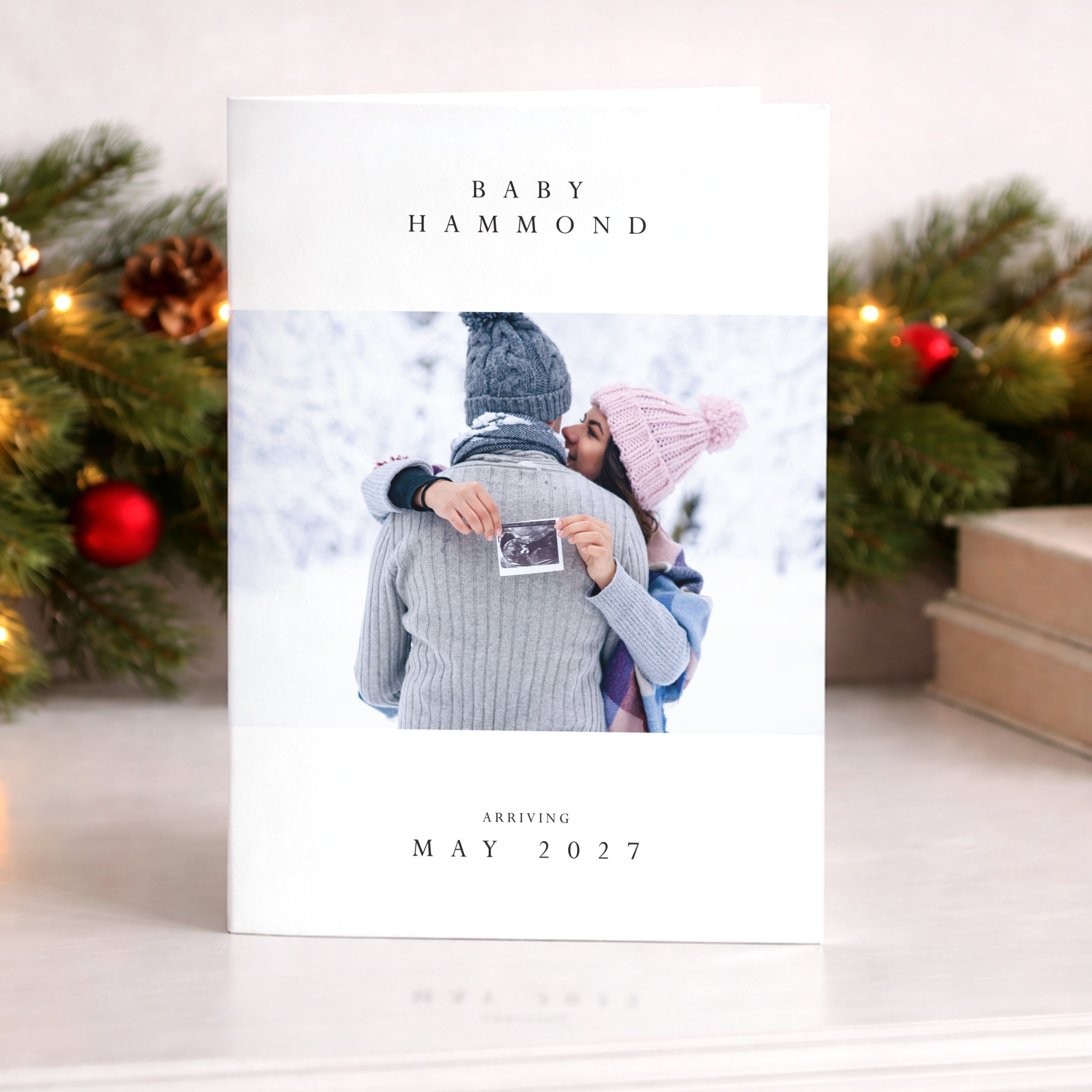 Baby announcement card with a couple holding a ultrasound photo, surrounded by Christmas decorations.