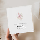 Greeting card with floral design and text for Mother's Day held by a hand on a neutral background